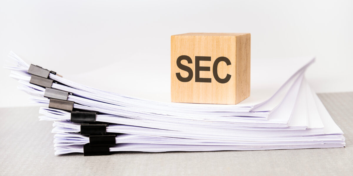 a wooden cube with a text SEC on a stack of documents grey table white background - California Business Attorneys | Oakland CA Wooden cubes that say SEC on top of a stack of papers.